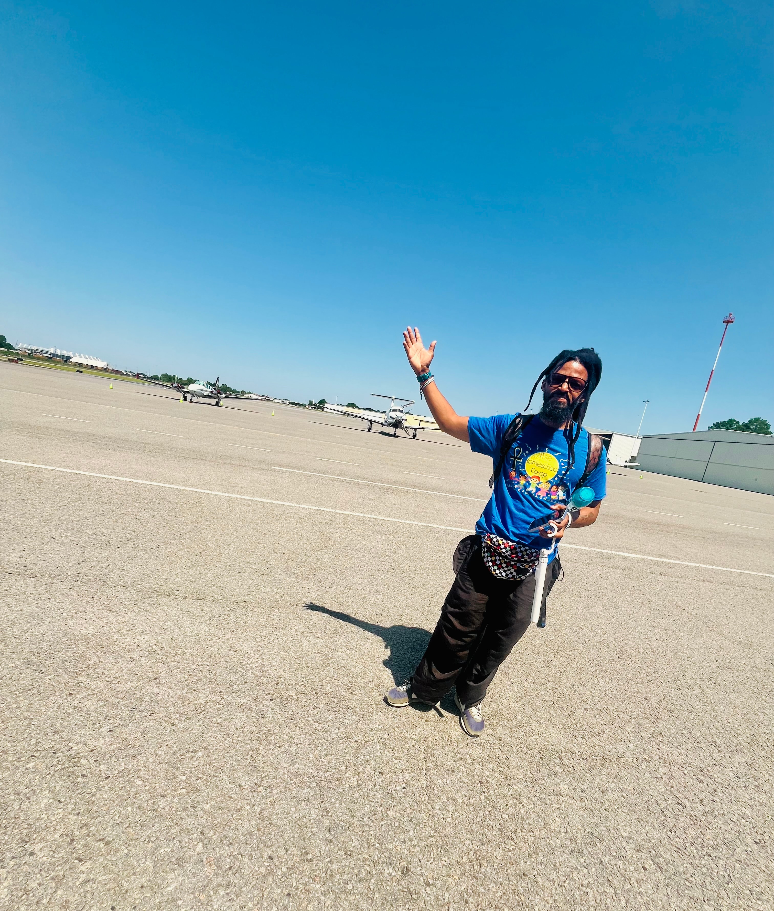 Co-op parent waving on the airport tarmac with planes in the background
